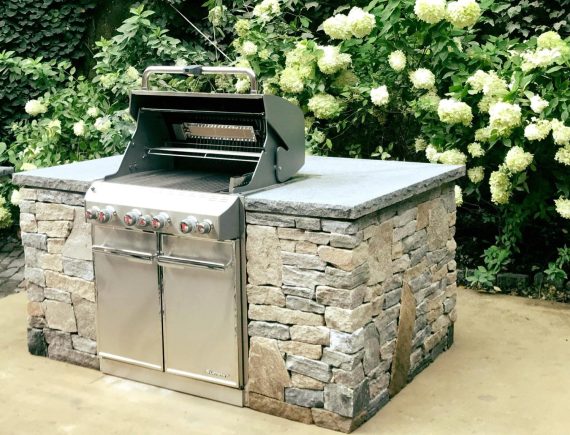 built-in stone outdoor grill surrounded by hydrangeas