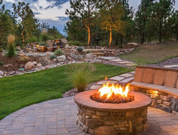 stone patio with bench and fire pit, retaining wall and garden beds in background